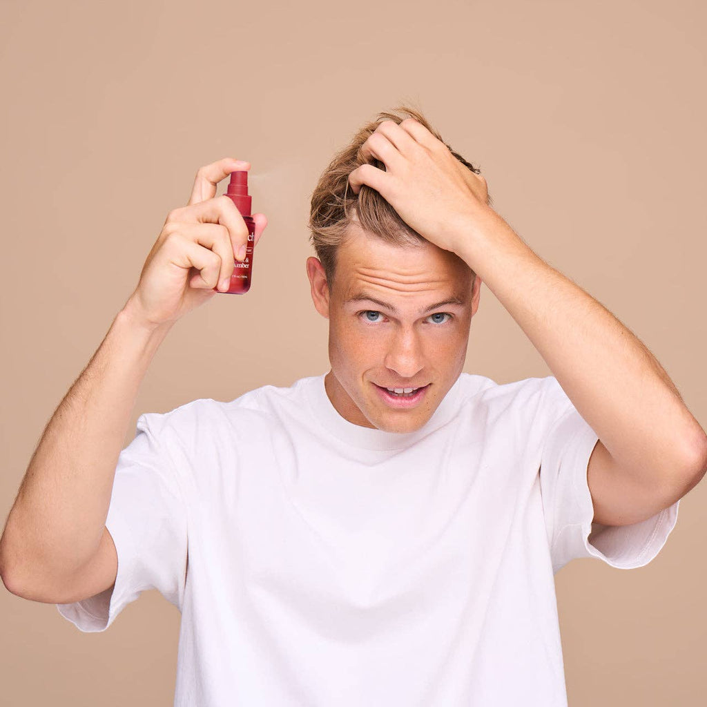 Man applying hair product with a spray bottle on a beige background