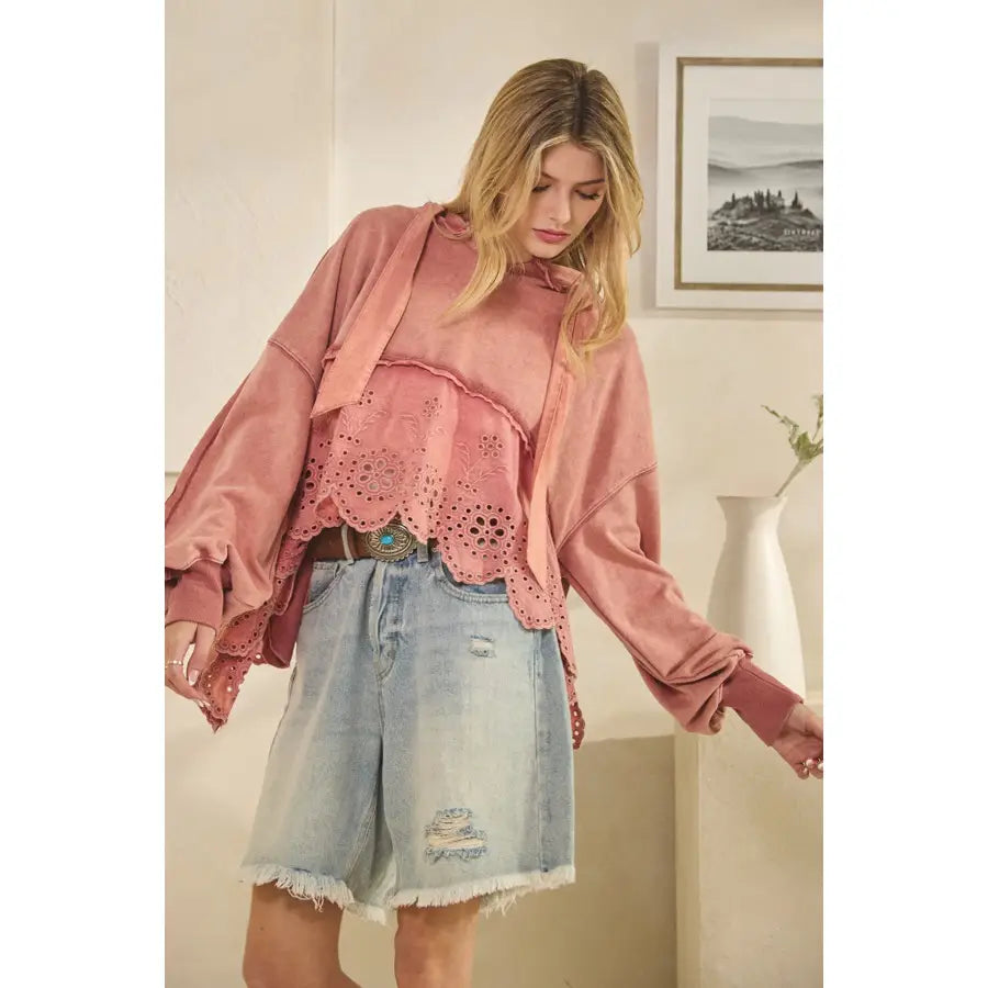 Woman wearing a pink oversized sweatshirt and denim shorts indoors.