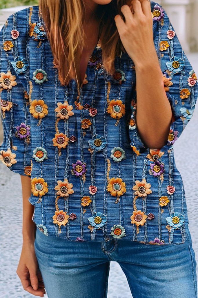 Woman wearing a blue floral V-neck blouse with roll-up sleeves, styled casually with denim.