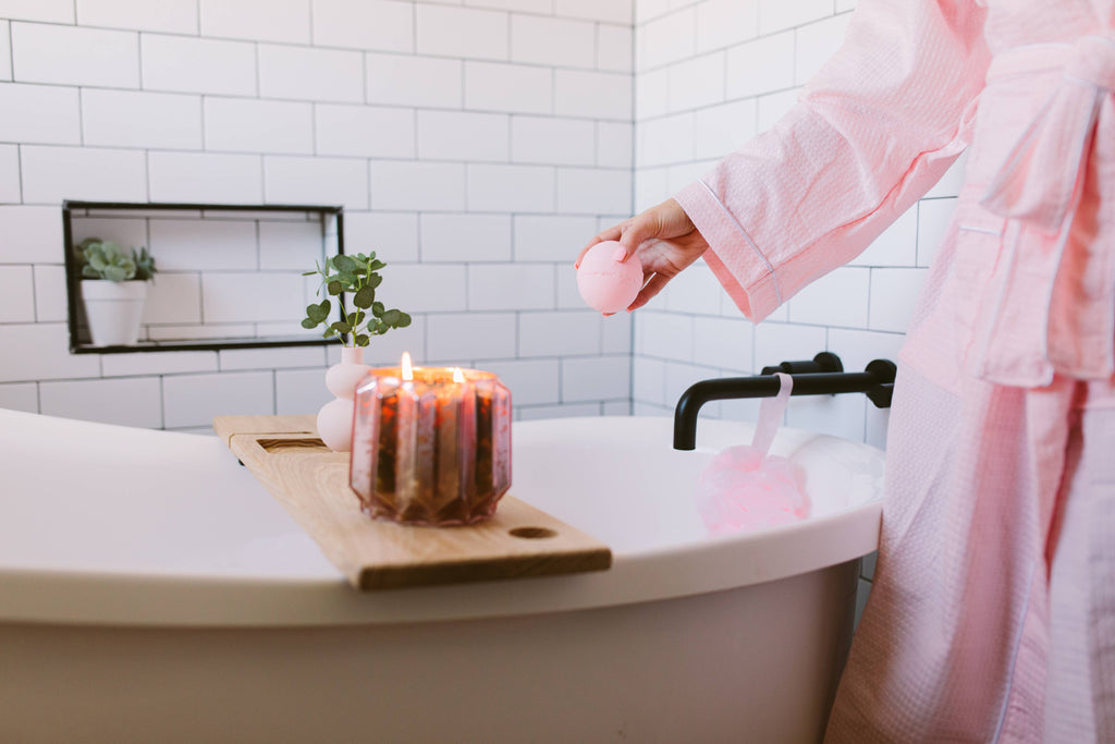 Person in a pink robe by a bathtub with a candle on a wooden board