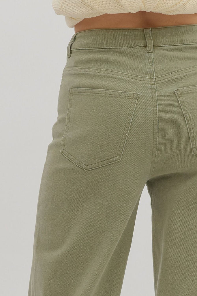 Olive green ankle-length pants with wide cuffed hems and classic jean-style pockets, styled with a cropped cream sweater and beige platform clogs.