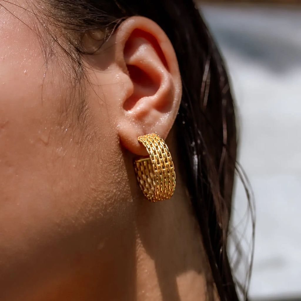 Close-up of an ear wearing a gold hoop earring with blurred background