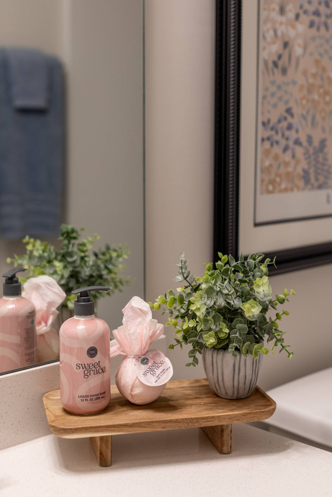 Bathroom setting with pink bottles, a plant, and a wooden tray.