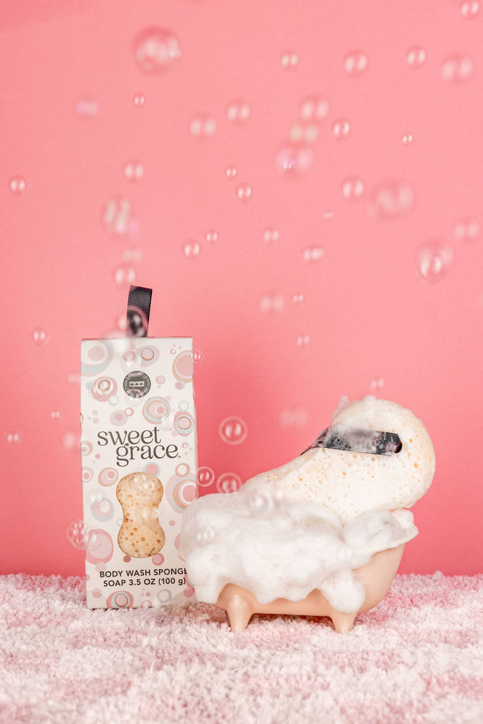Body wash sponge with packaging labeled 'sweet grace' on a pink background with bubbles.