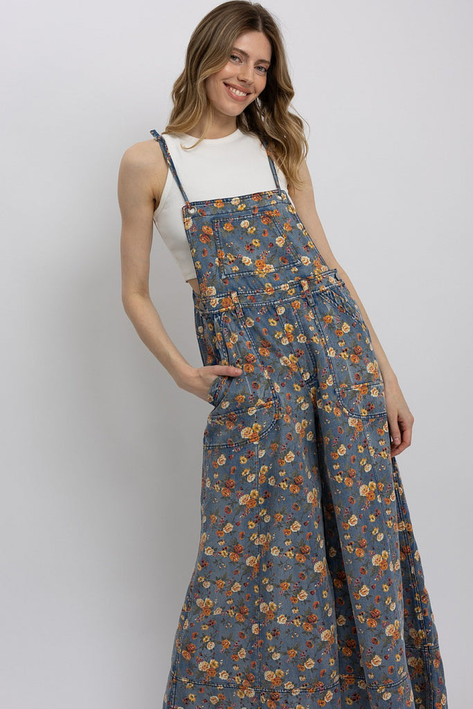 Woman wearing lightweight floral wide-leg denim overalls with adjustable straps, styled over a white tank top.