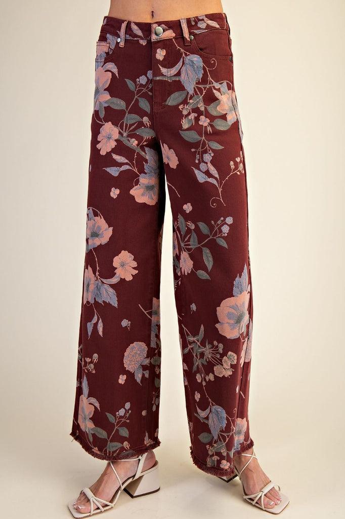 Model wearing Easel Calluna floral twill pants in burgundy with soft pink and blue botanical print, featuring high waist and straight leg silhouette.