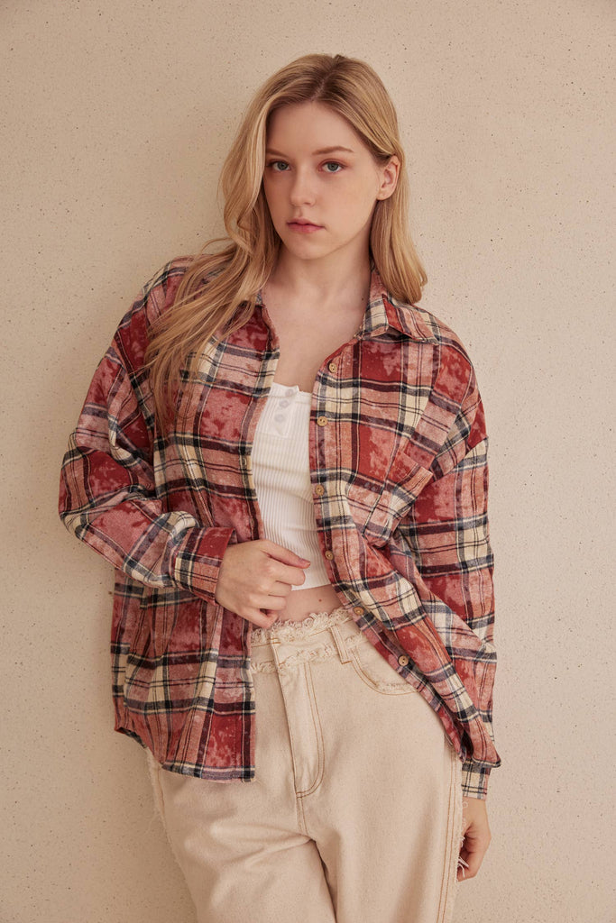 Woman wearing a plaid shirt over a white top and beige pants against a beige wall.