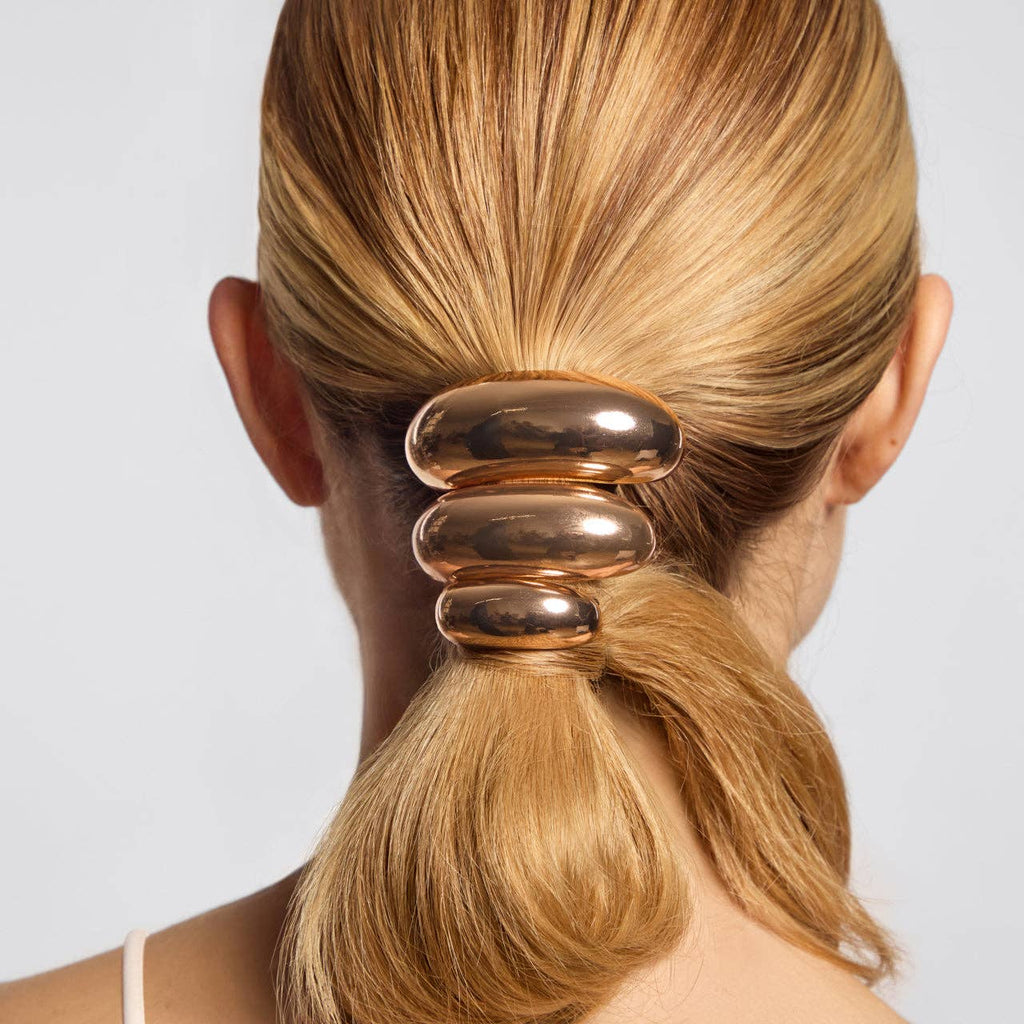 Gold hair tie on a person's ponytail against a plain background