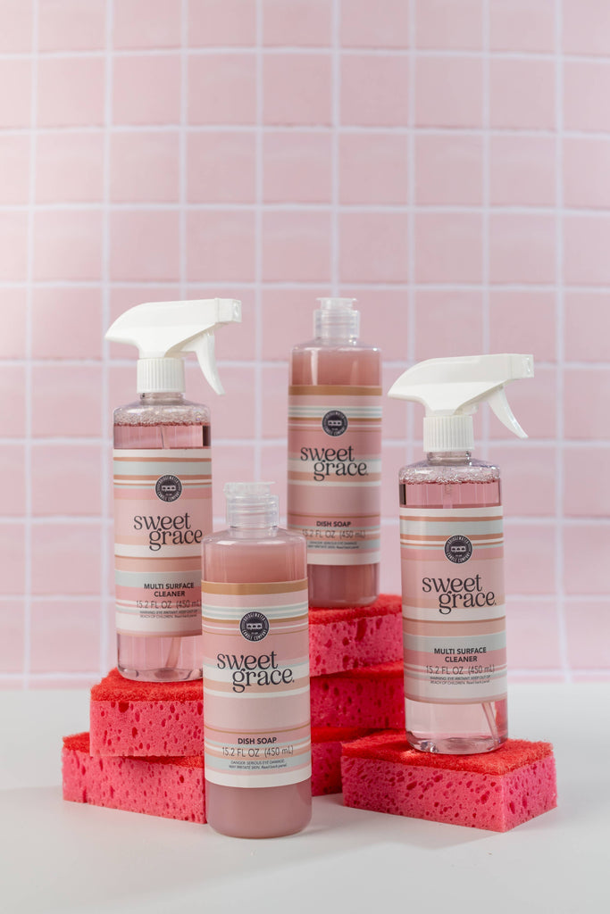Bottles of Sweet Grace cleaning products with sponges on a pink tiled background
