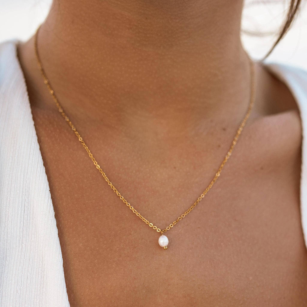 Gold necklace with a pearl pendant on a person wearing a white top.