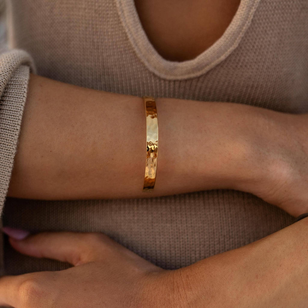 Gold bracelet on a wrist with a neutral background