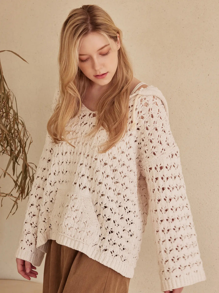 Woman wearing an ivory hooded crochet sweater with boat neckline and front pocket, styled with corduroy pants for a cozy boho look.
