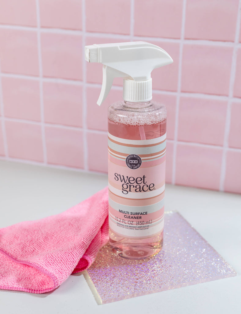 Bottle of Sweet Grace multi-surface cleaner with a pink towel and glittery surface cleaner on a pink tiled background