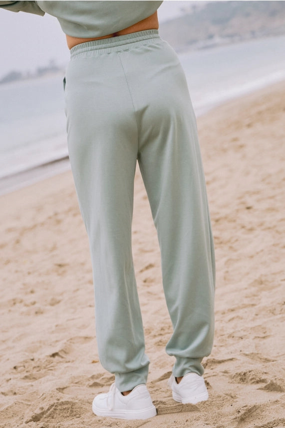 Person wearing light gray sweatpants on a sandy beach.