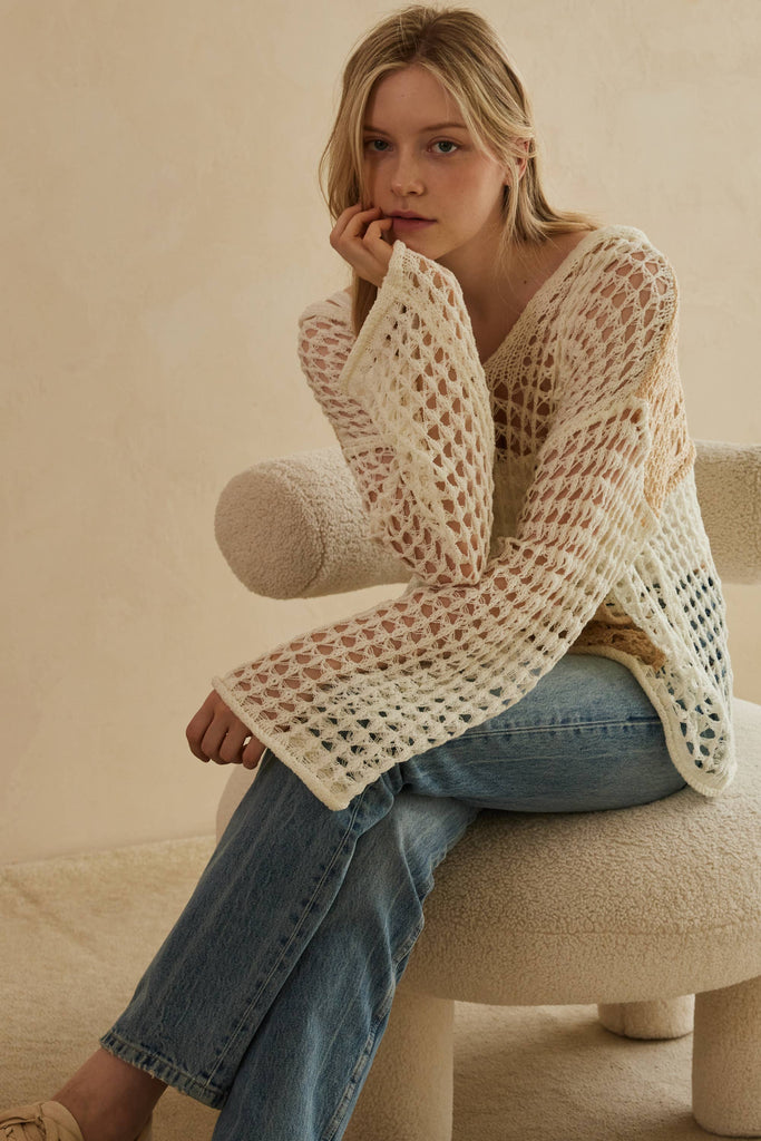 Woman wearing a beige crochet sweater and blue jeans sitting on a beige chair.