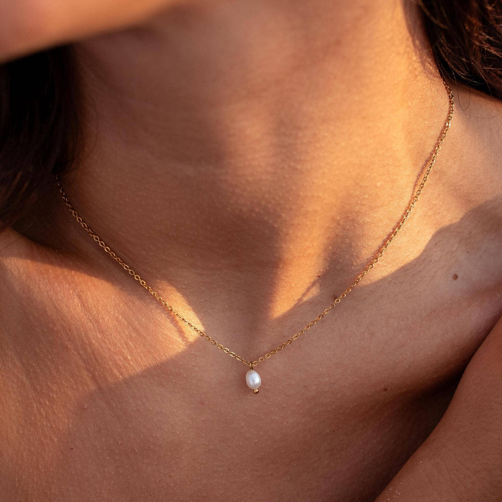 Gold necklace with a pearl pendant on a person's neck, sunlit background