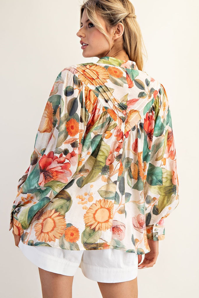 Model wearing a billowy, floral-printed blouse with balloon sleeves, a button front, and a high-low hem, styled with high-waisted white shorts.