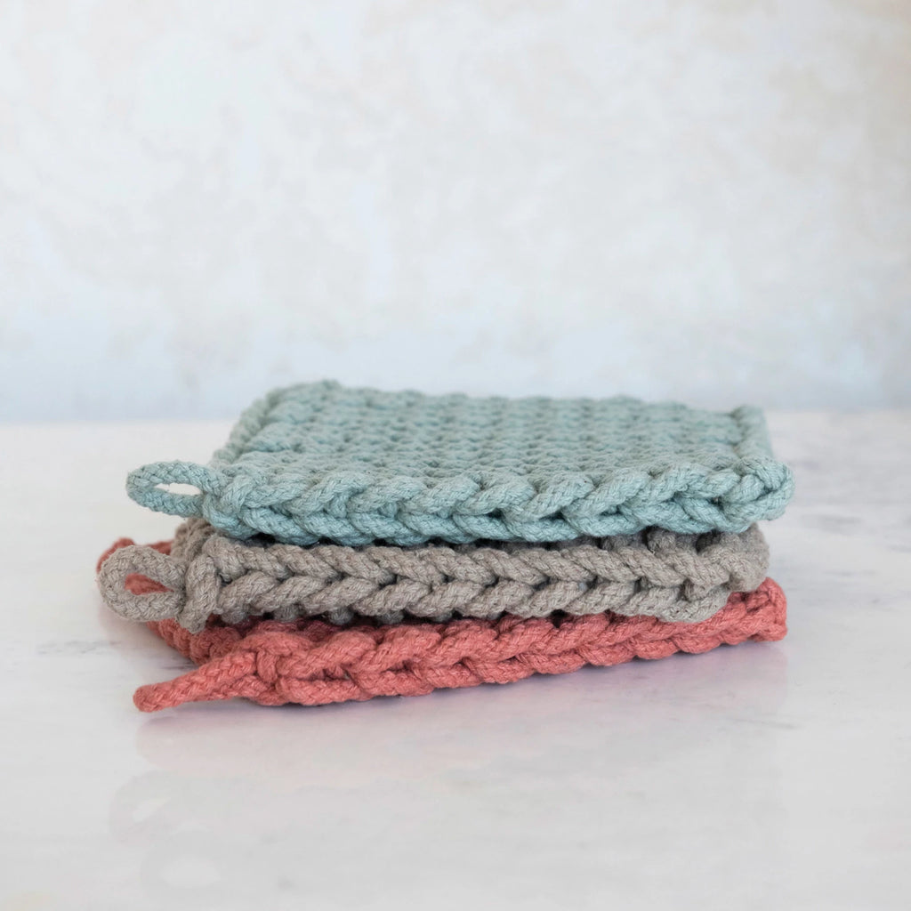 Stack of three knitted washcloths in blue, gray, and pink on a white background