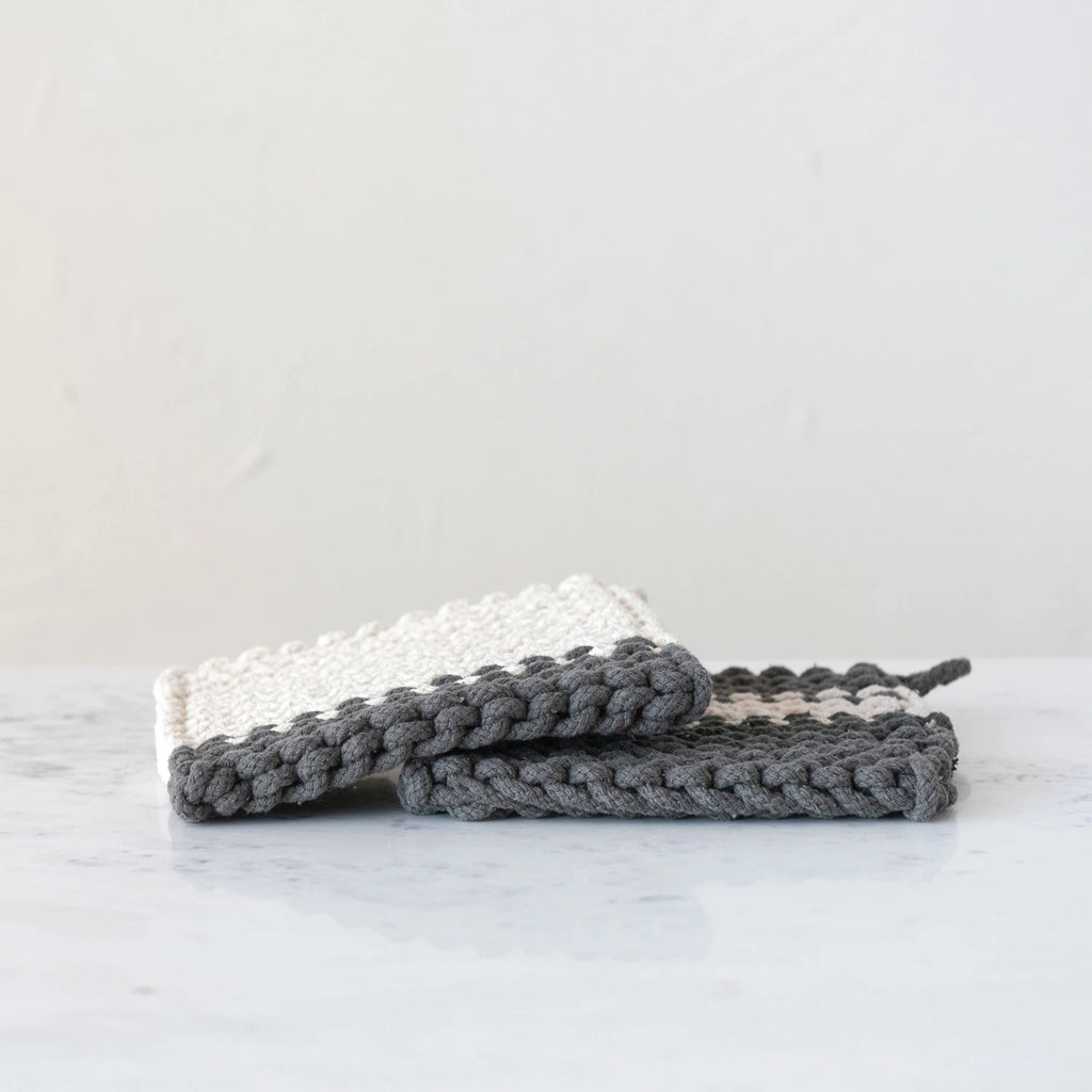 Two folded knitted items, one white and one gray, on a marble surface with a light gray background.