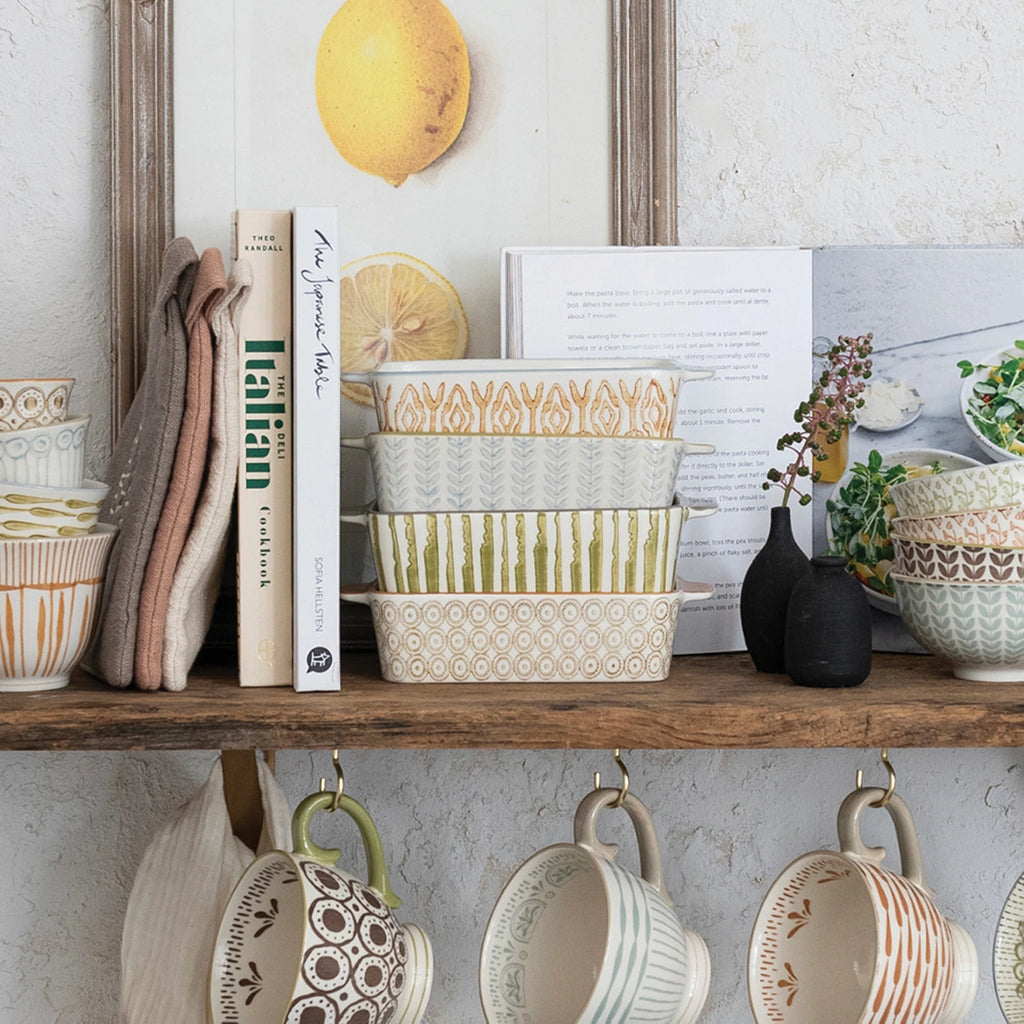 Wooden shelf with patterned bowls, books, and hanging mugs against a light wall.