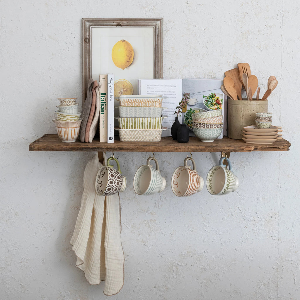 Wooden shelf with mugs, books, and kitchen utensils against a white brick wall.