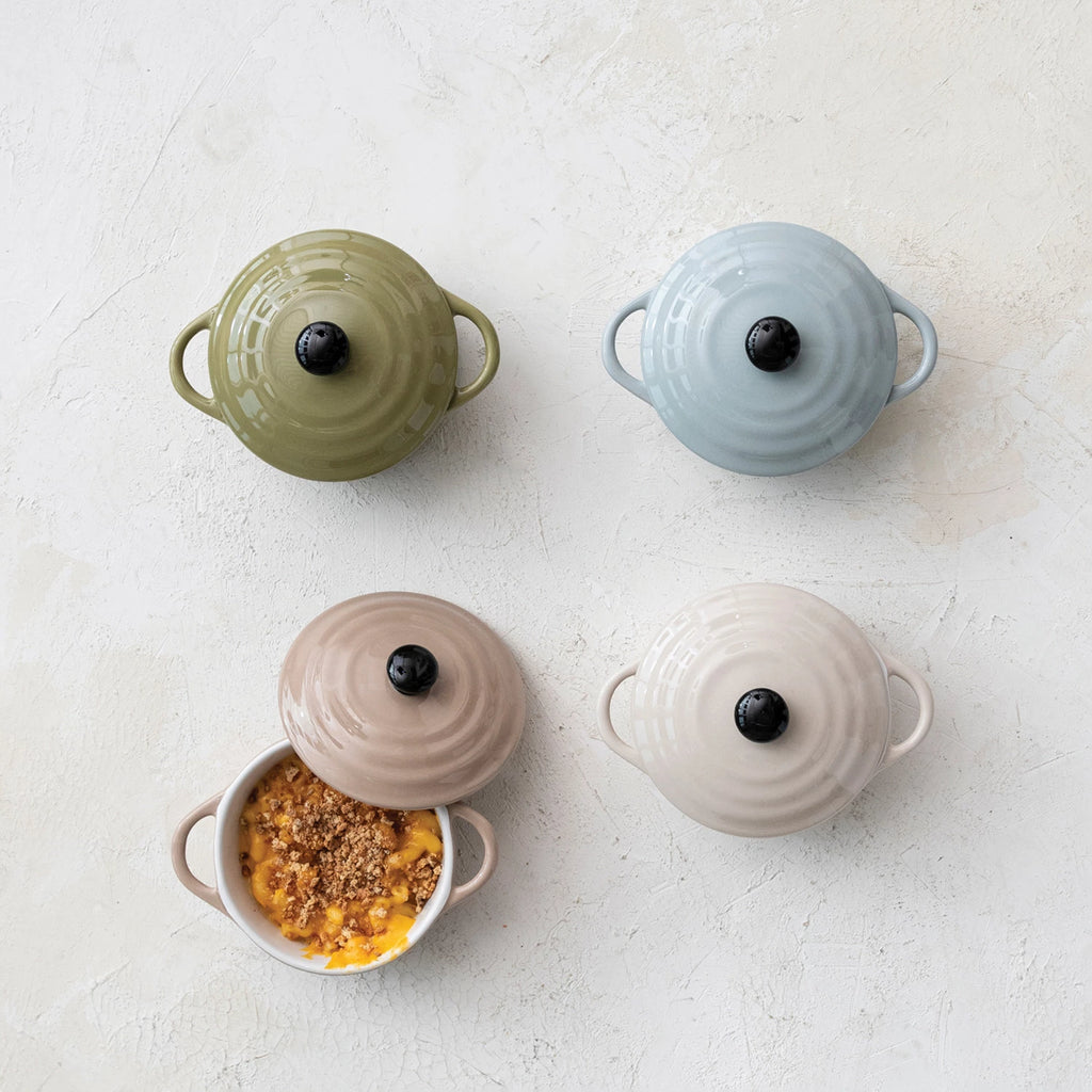 Four ceramic cookware pots in different colors on a light surface