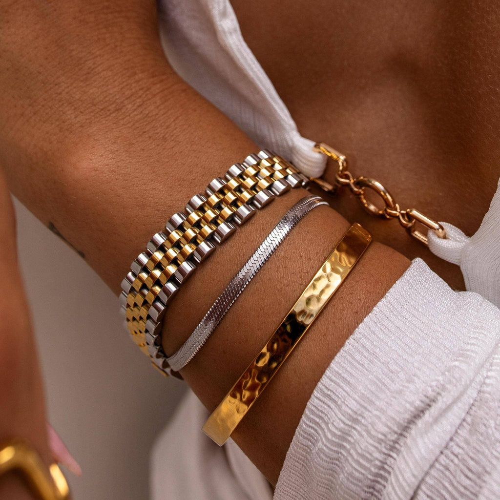 Close-up of a wrist wearing multiple gold and silver bracelets on a neutral background