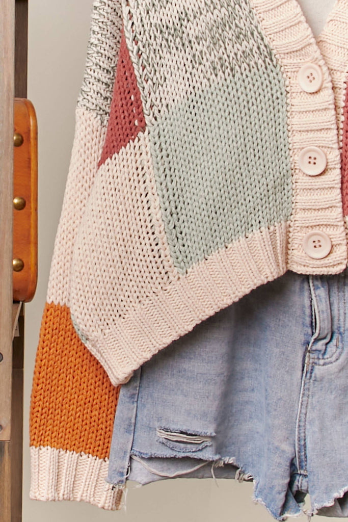 Colorful knitted cardigan with geometric pattern over denim shorts on a wooden chair.
