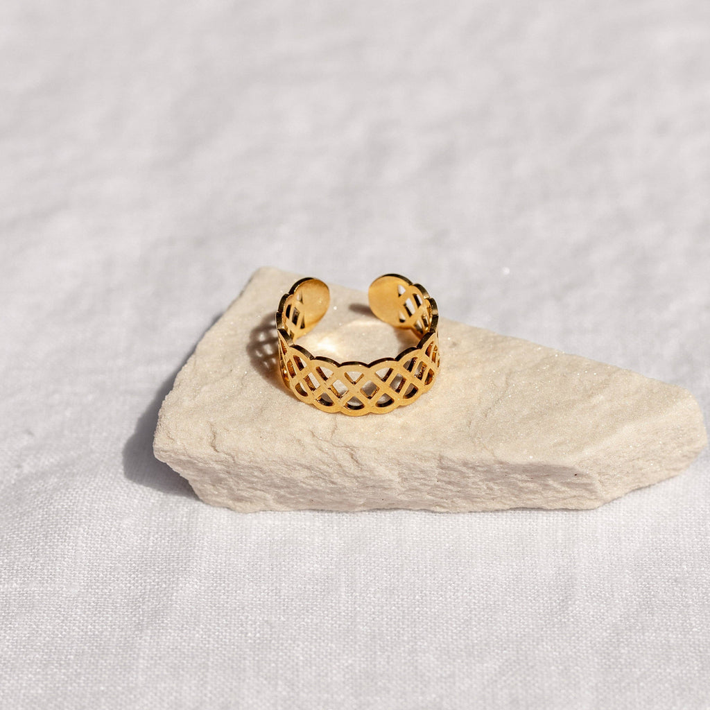 Gold ring with intricate design on a light stone surface