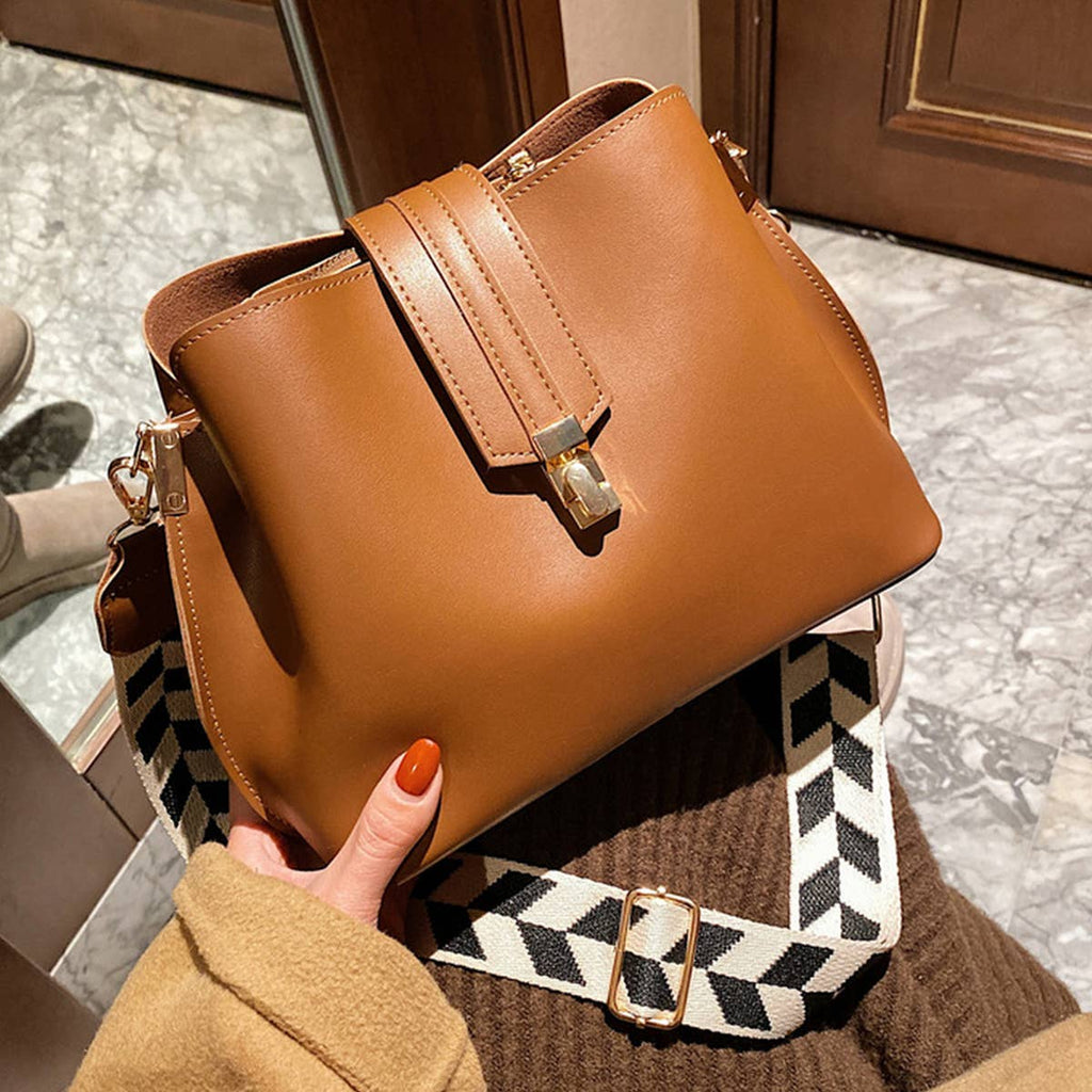 Brown handbag with a checkered strap held by a person on a marble floor.