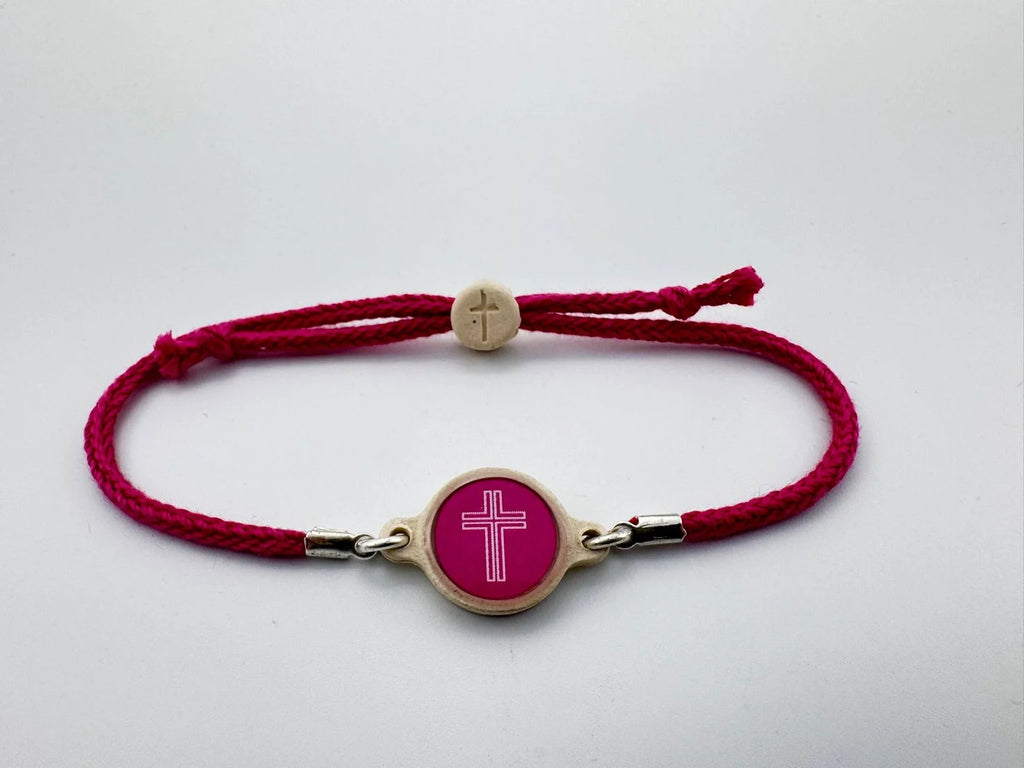 Red bracelet with a gold clasp and pink circular charm featuring a white cross on a light gray background.