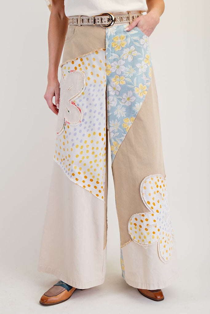 Beige wide leg pants with mixed floral patches, raw edges, and a relaxed fit. women's boutique easel