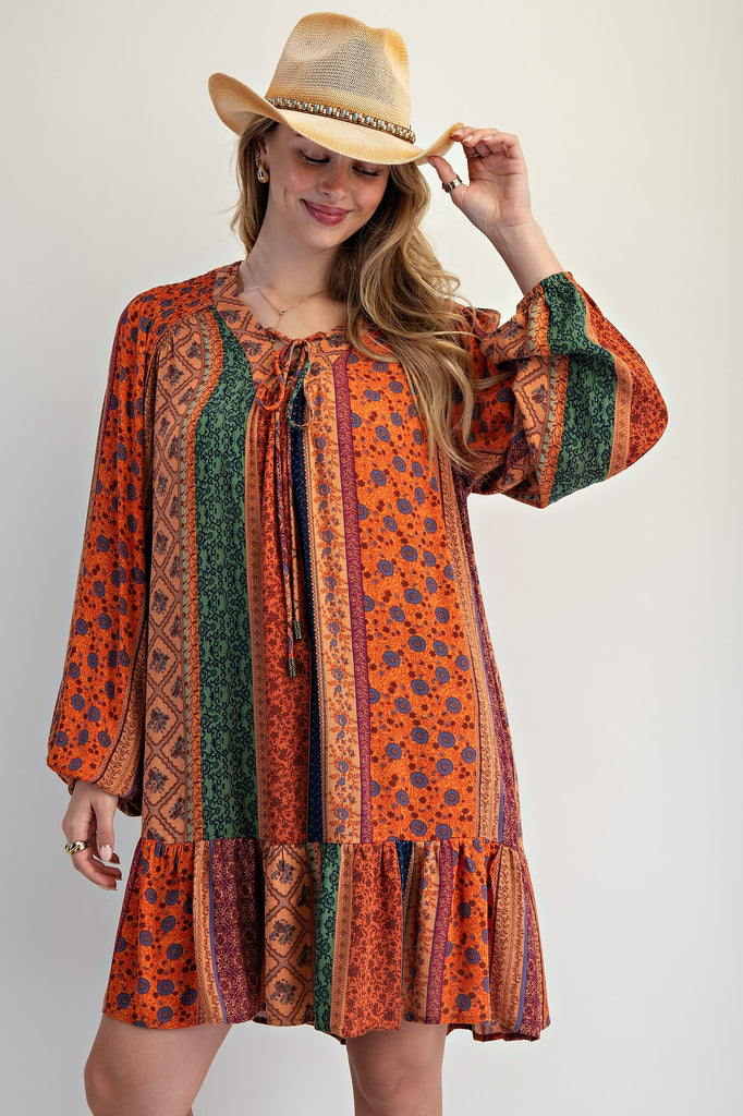 Pumpkin-colored patchwork dress with long balloon sleeves, ruffled hem, and boho floral prints. missouri boutique easel