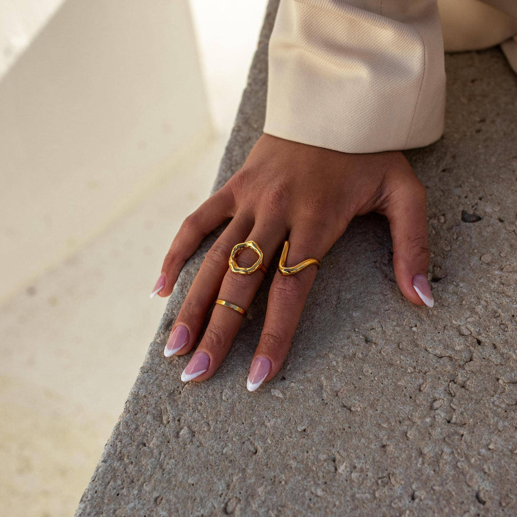 A gold-colored hammered metal ring on a person's finger, displaying an open circle design symbolizing new beginnings.

