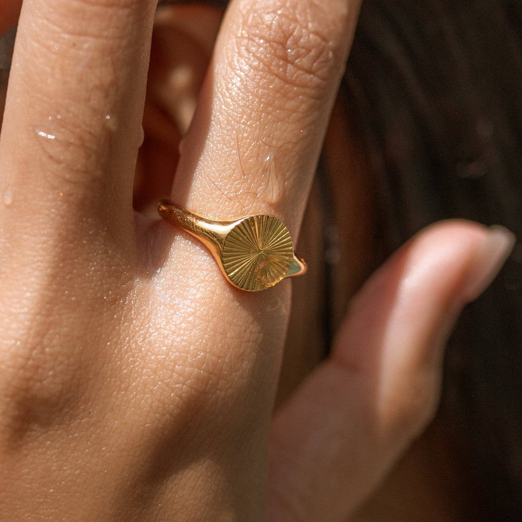 Close-up of a hand wearing a gold ring with a leaf design.