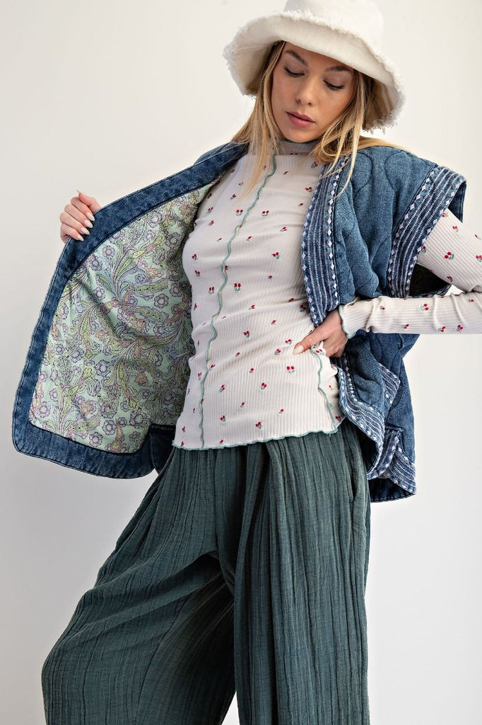 Woman wearing a blue patterned shawl over a white blouse with red details and green pants on a white background