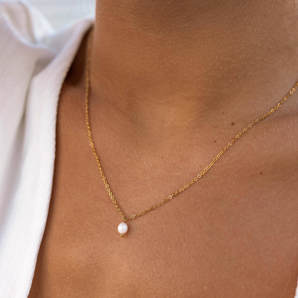 Gold necklace with a pearl pendant on a person wearing a light-colored top.