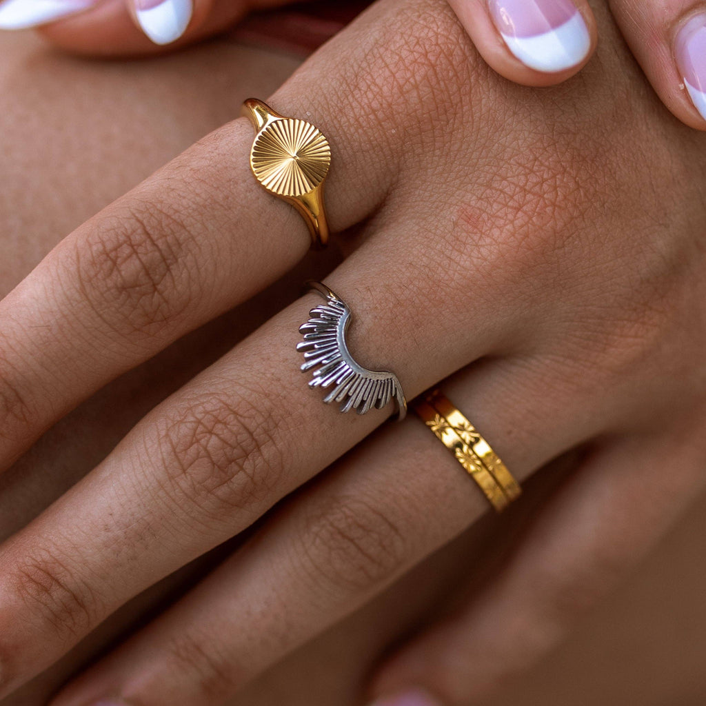 Close-up of a hand wearing three gold and silver rings on a neutral background