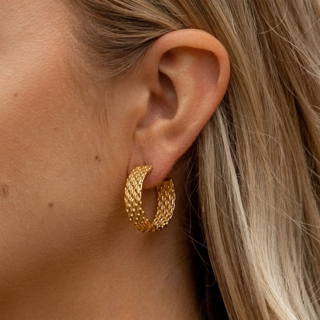 Gold hoop earrings worn by a person with blonde hair.