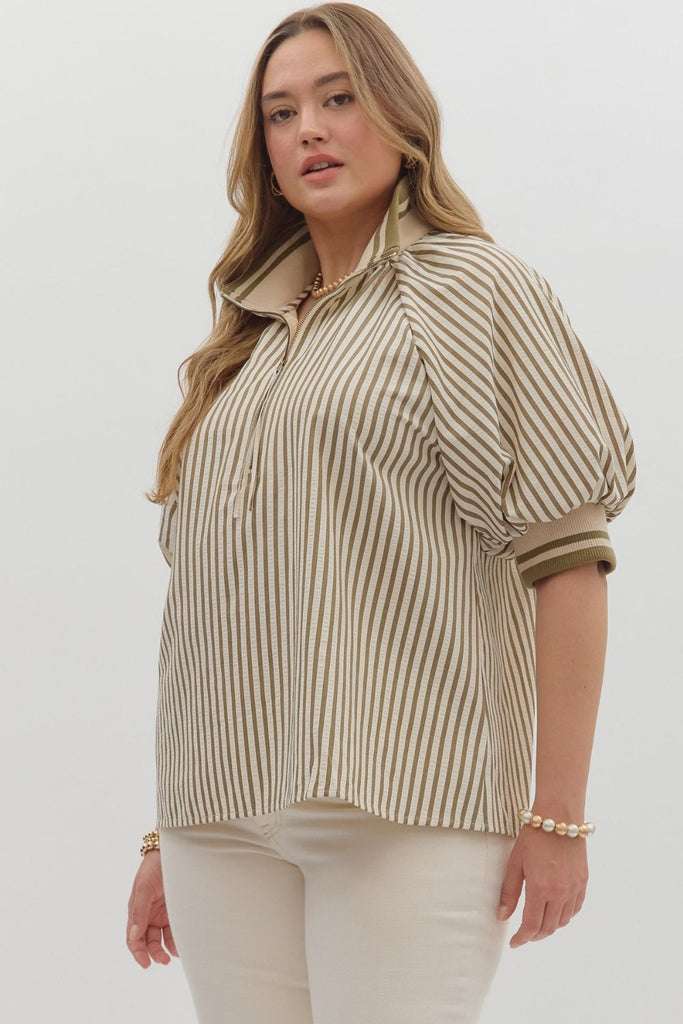 A woman poses at a slight side angle, wearing a short-sleeved striped top with puff sleeves and a half-zip collar. The top features olive and white vertical stripes with ribbed cuffs. Her head is turned slightly