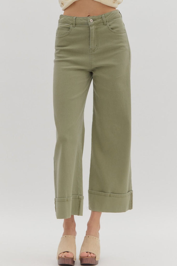 Olive green ankle-length pants with wide cuffed hems and classic jean-style pockets, styled with a cropped cream sweater and beige platform clogs.
