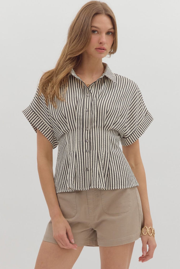 A woman wearing a vertical black and white striped short-sleeve blouse with a collar and button-down front, paired with tan shorts.