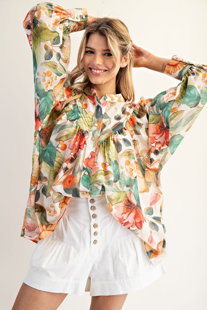 Model wearing a billowy, floral-printed blouse with balloon sleeves, a button front, and a high-low hem, styled with high-waisted white shorts.