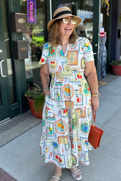 White midi dress with colorful fruit print, tiered skirt, ruched waist, and notched neckline. women's boutique easel
