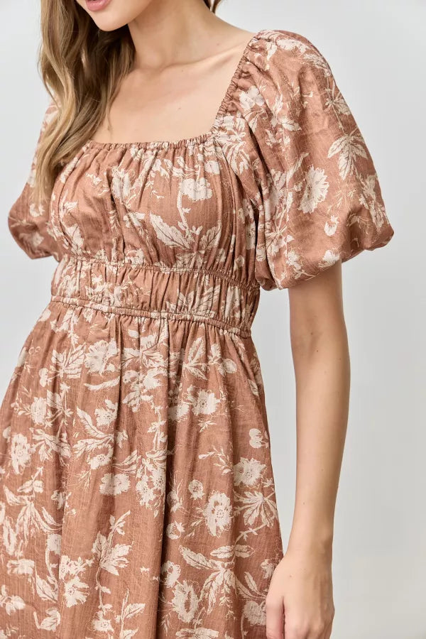 Model wearing Isola Floral Textured Midi Dress in terracotta with cream floral print, puff sleeves, and smocked waist.