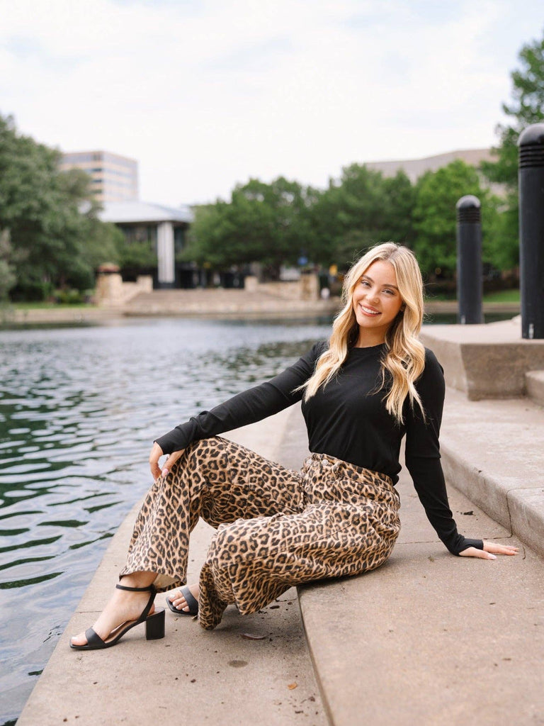 Woman wearing a black ribbed long sleeve top paired with lepord jeans.