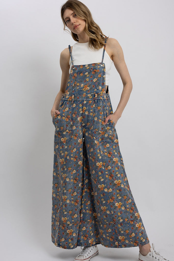 Woman wearing lightweight floral wide-leg denim overalls with adjustable straps, styled over a white tank top.