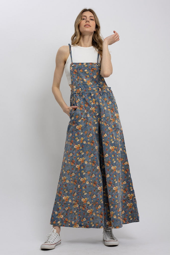 Woman wearing lightweight floral wide-leg denim overalls with adjustable straps, styled over a white tank top.