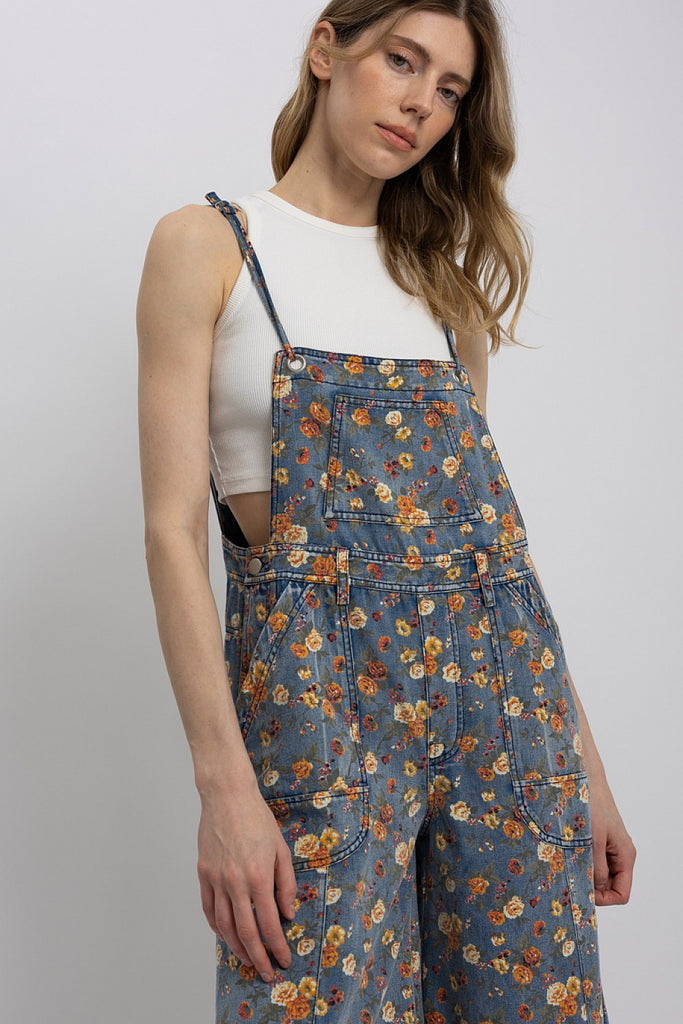 Woman wearing lightweight floral wide-leg denim overalls with adjustable straps, styled over a white tank top.