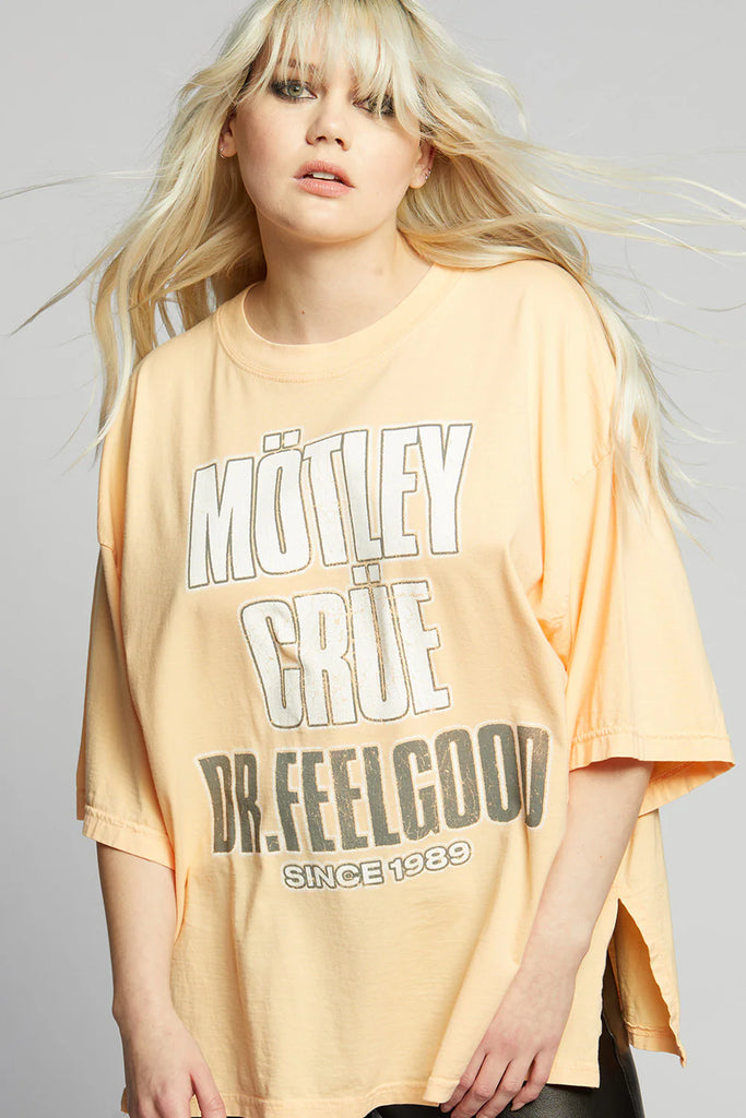 Person wearing a yellow oversized t-shirt with 'Mötley Crüe Dr. Feelgood' text on a plain background